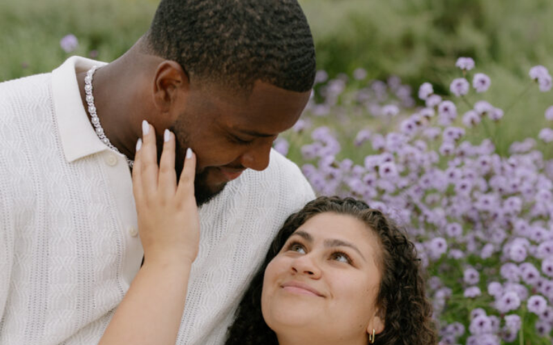 This image captures a joyful moment between Kobie Turner and his fiancée, Alissa Villanueva, as they smile at each other. The photo highlights the love and happiness between the couple, with both sharing an intimate and warm moment.