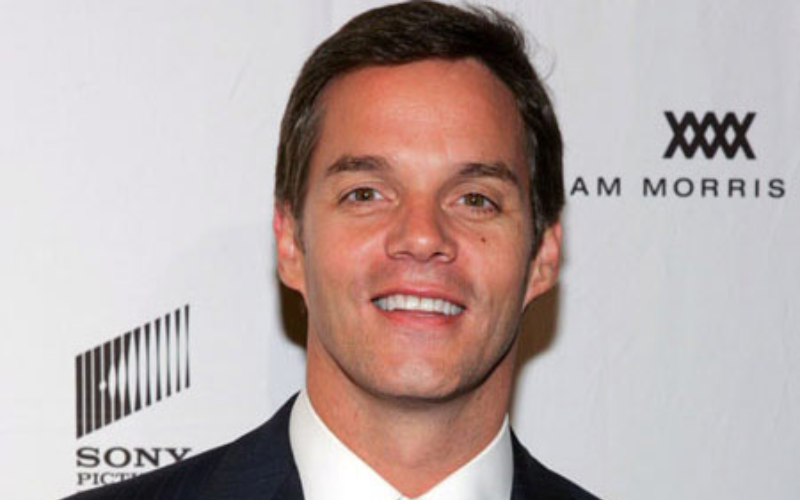 This image features Bill Hemmer smiling confidently in a sharp black suit, with the question "Who is Bill Hemmer's Wife?" prominently placed next to him. The image reflects his approachable yet professional demeanor, drawing attention to the ongoing curiosity about his personal life and relationship status.