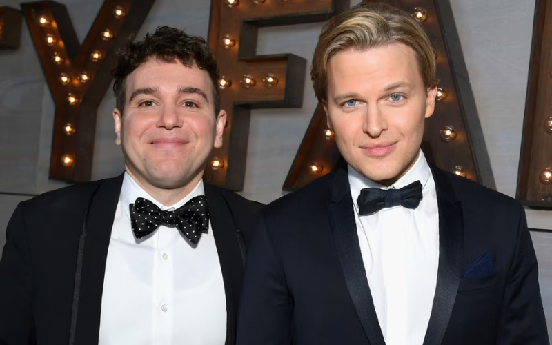 This image shows Jon Lovett and Ronan Farrow both dressed in suits, smiling together, representing their past relationship and the happy moments they shared as a couple.